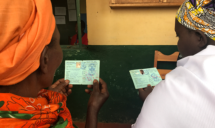 [Women waiting at a health center in Rwanda hold up their health insurance identification cards.] {Photo Credit: Denise Museminali/MSH}