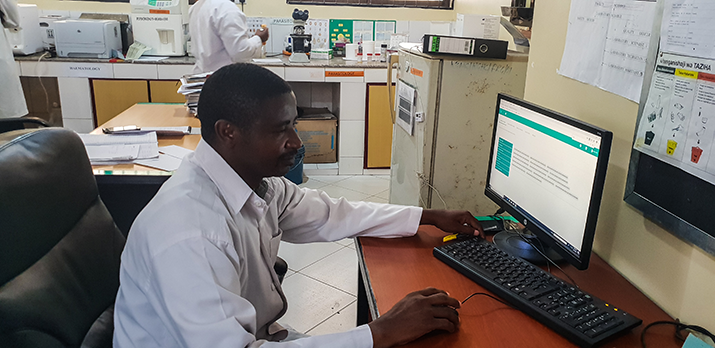 [Speratus Macarius, un técnico de laboratorio en el Centro de Salud Kigamboni en Tanzania, verifica una orden de prueba en el nuevo sistema de registros médicos electrónicos de la instalación.] {Crédito de la foto: Paul Bwathondi / MSH}