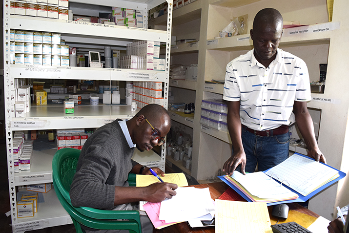 [Henry Oundo, UHSC staff member, reviews stock records with Opolot Grace, assistant inventory management officer at Princess Diana Health Center, Uganda.] {Photo credit UHSC staff/MSH}
