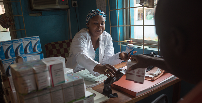 {Pharmacist Mary Yeesuf dispenses medicine to a patient in Minna, Nigeria. Photo Credit: Gwenn Dubourthournieu}