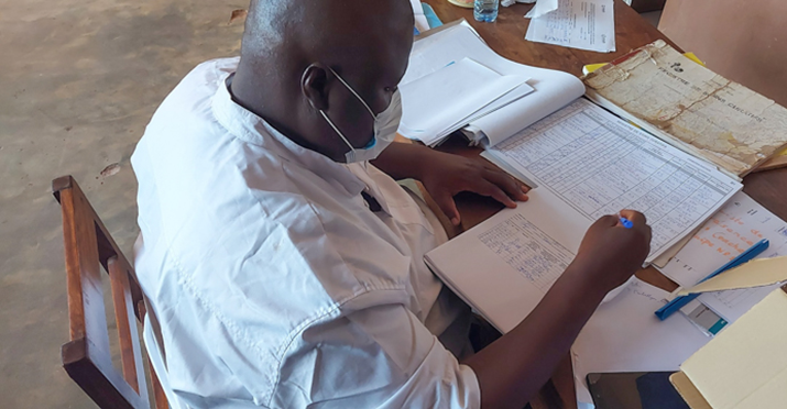 [Um treinador da zona de saúde Sakété-Ifangni, Plateau, contando o número de casos ativos de malária nos registros de saúde.] {Foto: Raphaël Gnonlonfoun, USAID Integrated Health Services Activity}