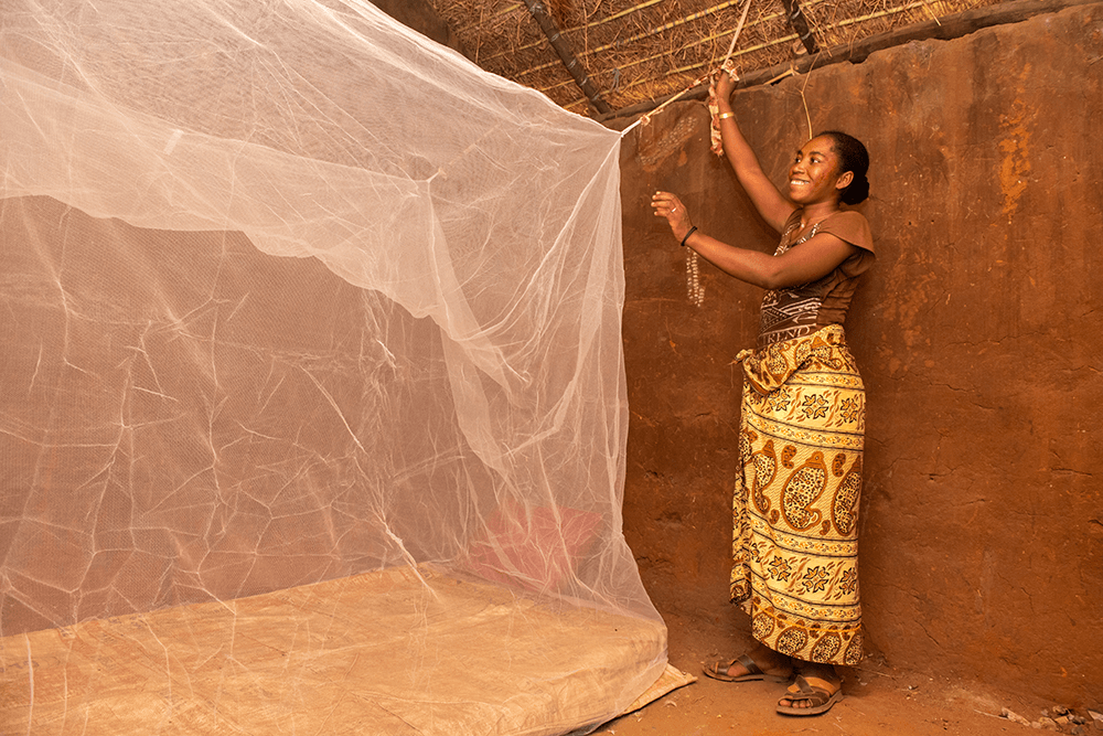 Une mère installe une moustiquaire dans sa maison à Madagascar