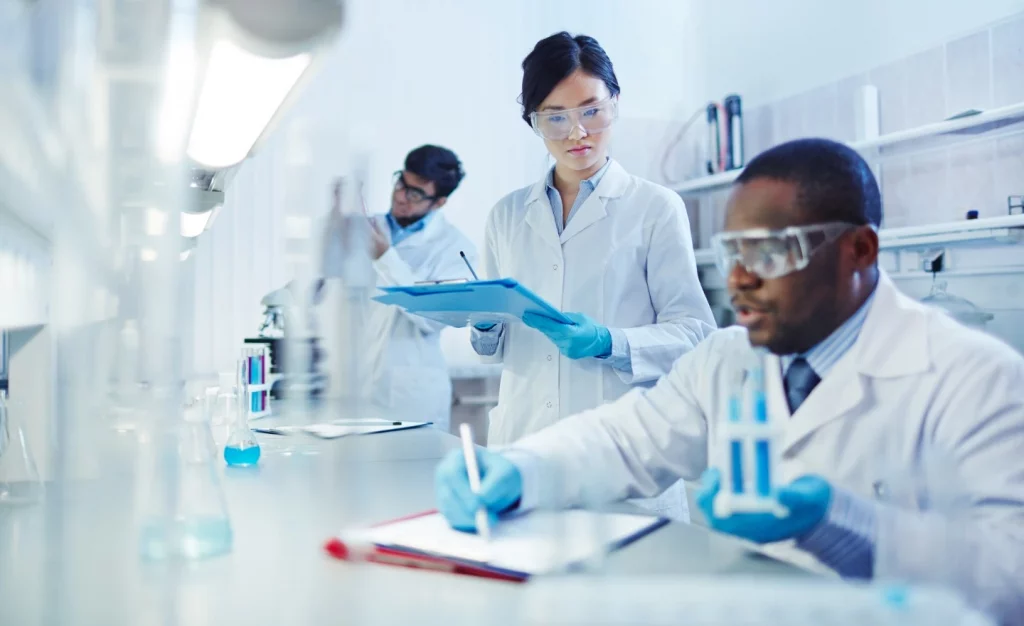 People working in a laboratory in white coats and goggles.
