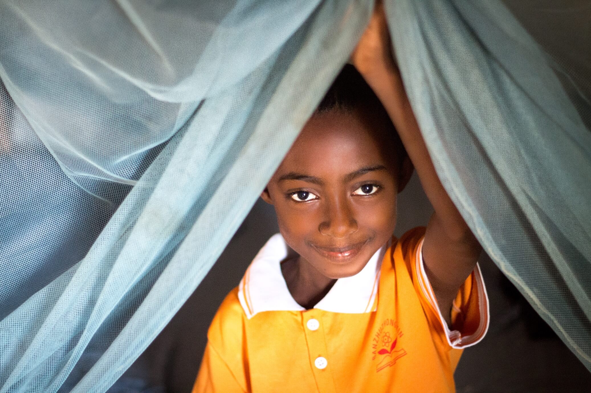 Child-peaking-out-from-under-a-new-bed-net-Madagascar