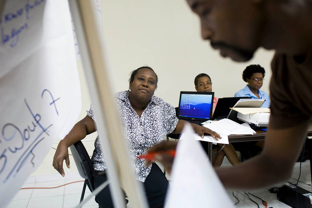 Dorvilier Gilbert effectue un exercice en classe lors d'un atelier de formation LMS, tandis que Marjery Applyrs, une responsable du programme LMS, encadre les leaders communautaires à Port-au-Prince, en Haïti. Photo de Dominic Chavez.