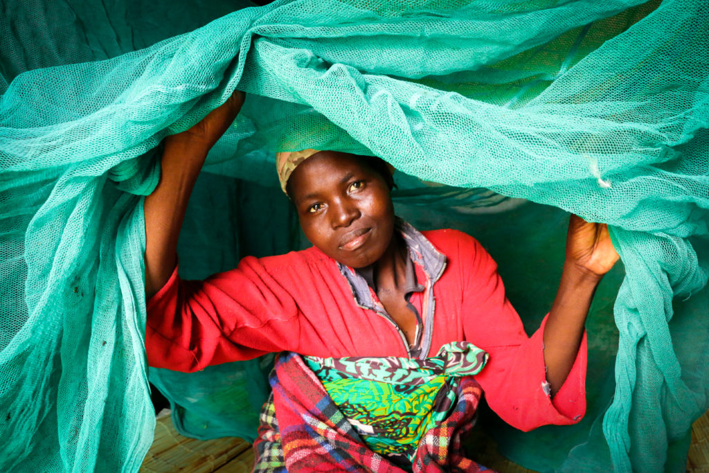 Woman in Malawi under a mosquito net over bed.