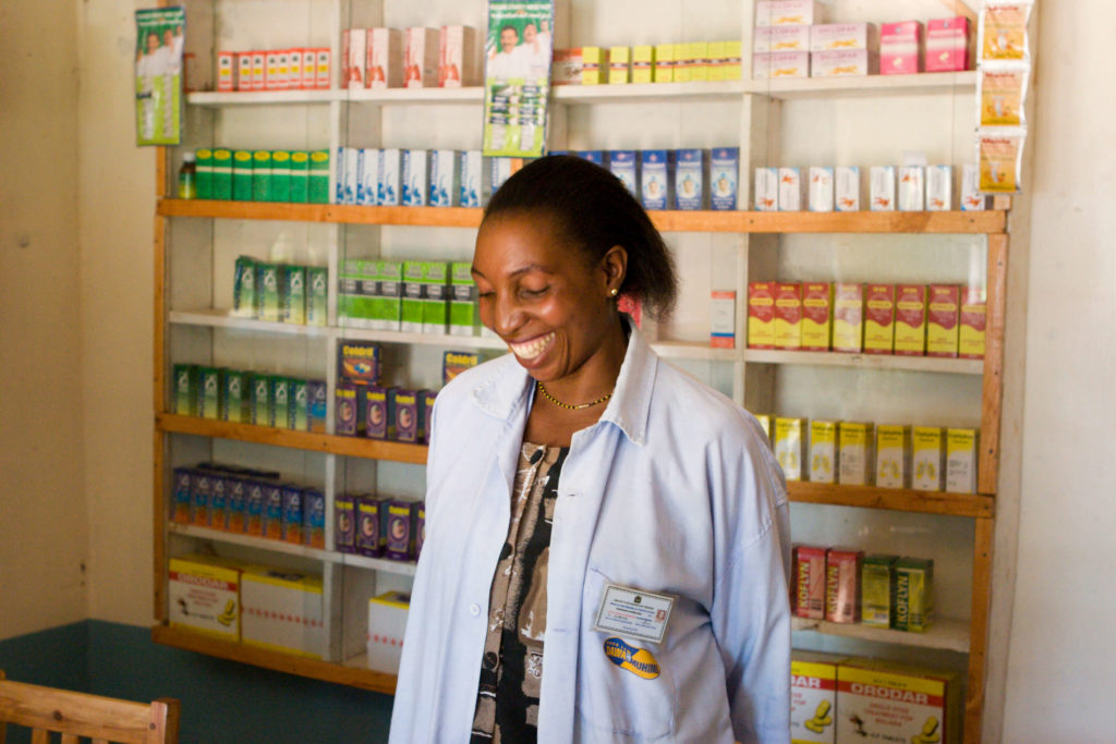 A pharmacist smiling in front of a medicine cabinet