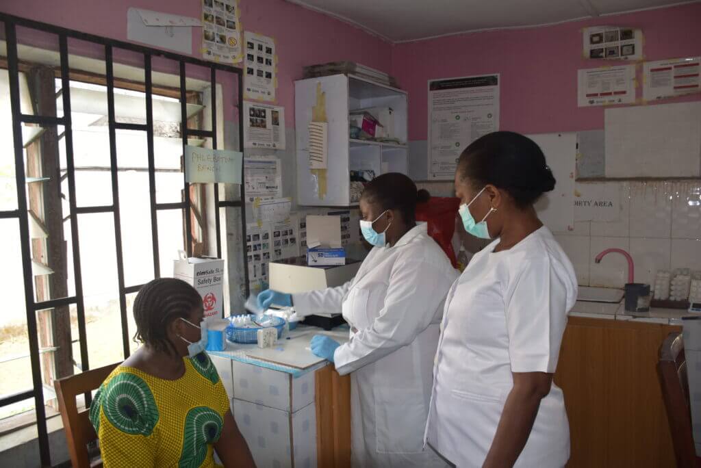 Mercy (right) supervising a laboratory staff member administering a malaria rapid diagnostic test. Photo credit: President’s Malaria Initiative for States (PMI-S)