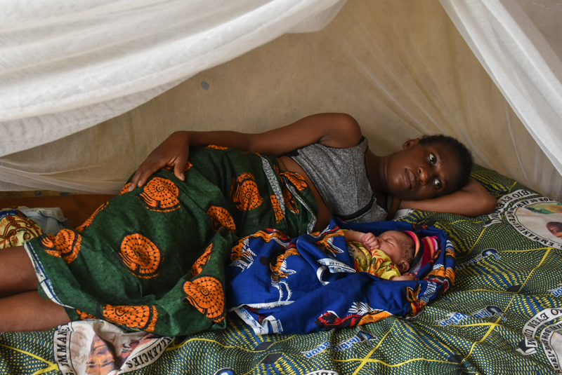 A woman lies with her baby under a mosquito net.