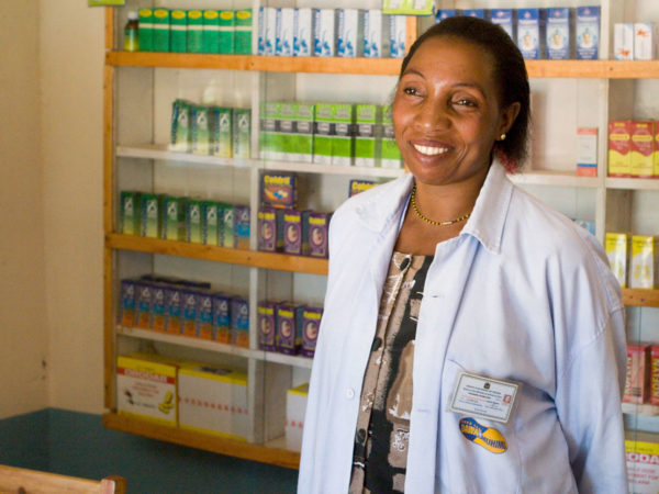 Eine Apothekerin mit einer Wand aus Medikamenten hinter sich in Tansania