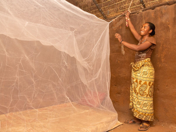 Uma mãe instalando um mosquiteiro tratado com inseticida em sua casa, Madagascar.