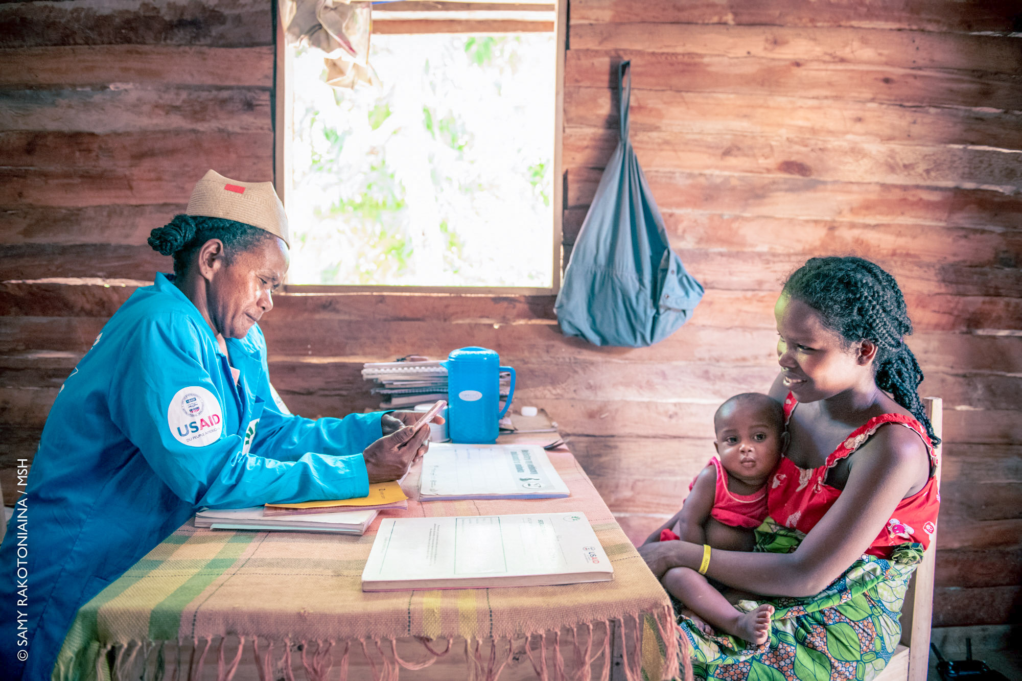 una mujer con un bebé en el regazo se sienta frente al escritorio de un voluntario de salud comunitario en un centro de salud de una aldea en Madagascar