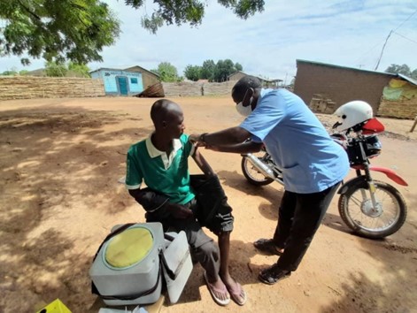 A health worker administers a COVID vaccine to a man under a tree in Benin.