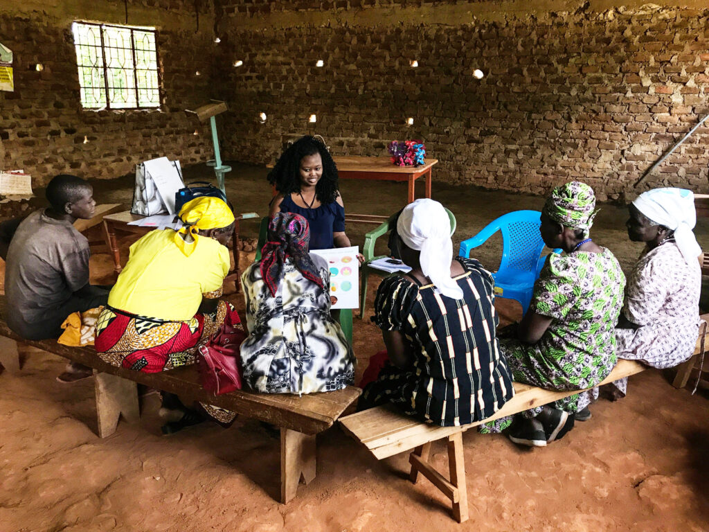 Six women sit on benches facing a health worker, who is providing information on how to maintain a safe and healthy pregnancy.