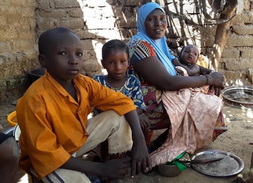 A woman sits on the ground with her children outside their mud brick home in Benin