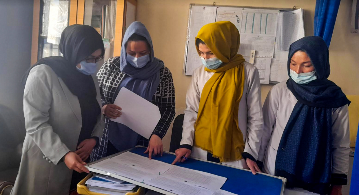 Four Afghani women in head scarves review a chart at a clinic in Afghanistan
