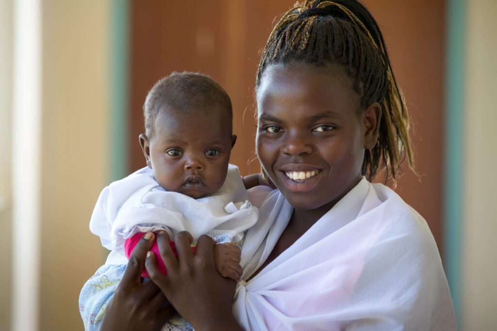 Eine kenianische Mutter und ihr neugeborenes Baby lächeln in die Kamera.