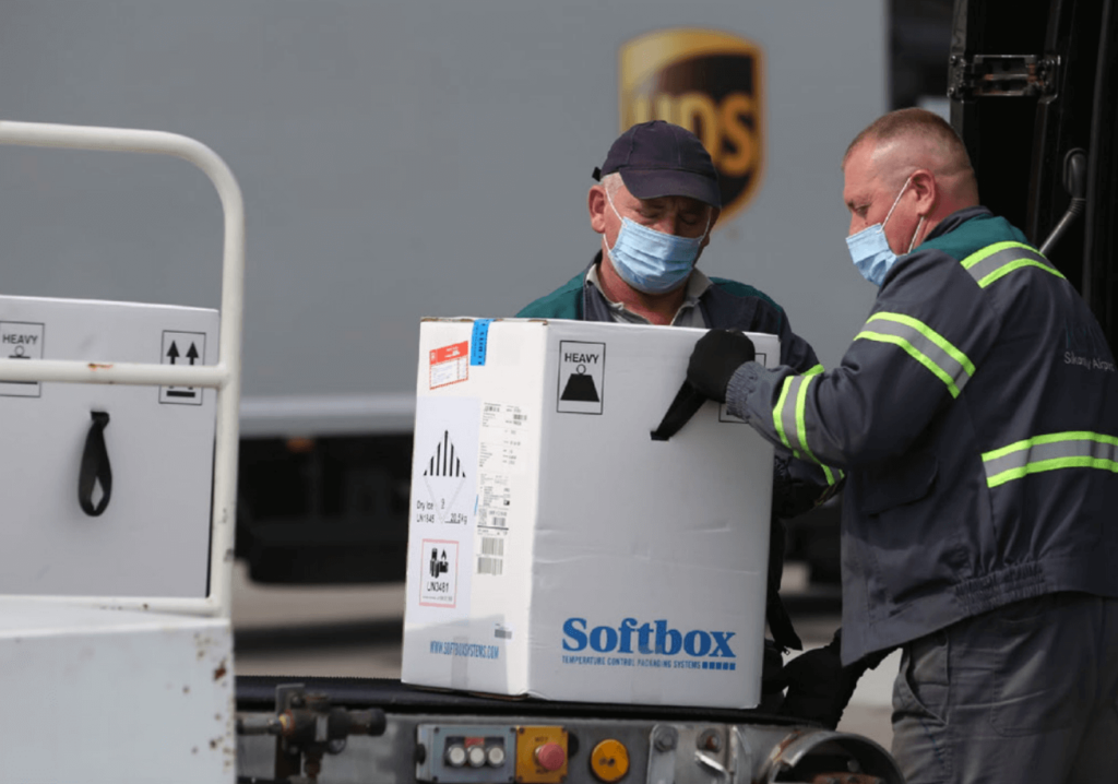 Dos hombres cargan cajas de medicamentos en una furgoneta.