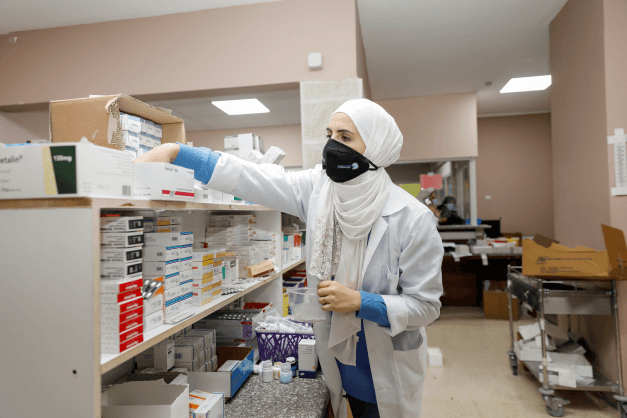 A pharmacist in a white hijab stocks a shelf