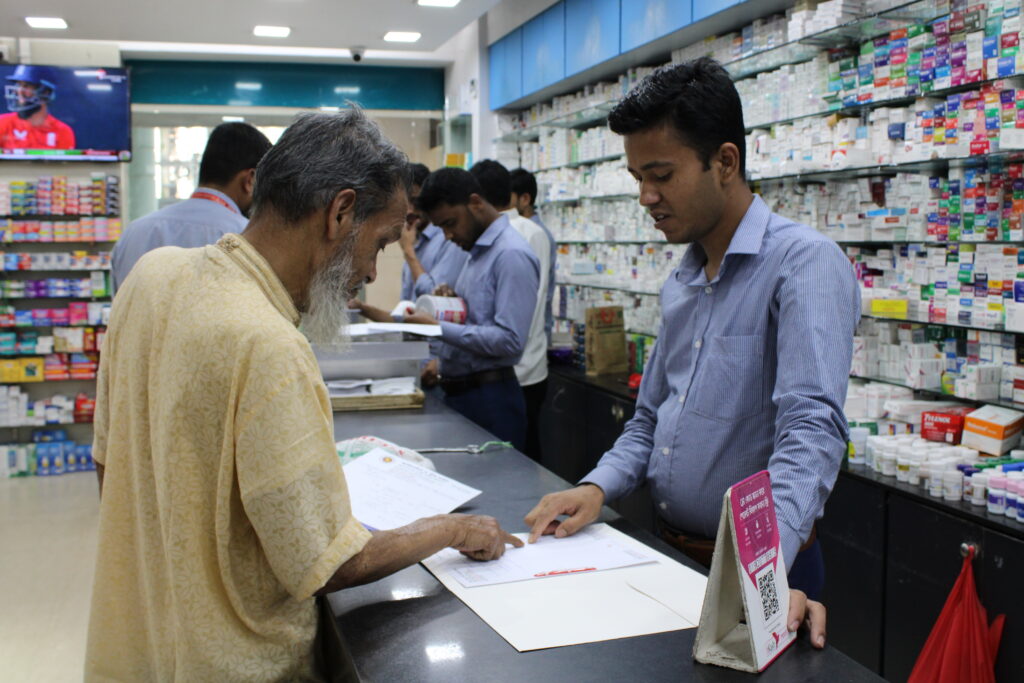 Ein geschulter Medikamentenspender in einem Arzneimitteleinzelhandel in Bangladesch berät sich mit einem Kunden. Bildnachweis: MSH