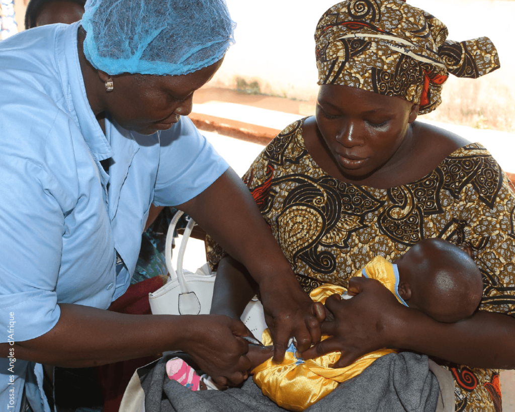 Um profissional de saúde no Benin administra uma vacina a um bebé que está nos braços da mãe.