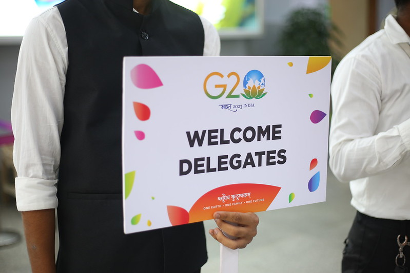 Man holds a sign with the G20 India 2023 logo that says "Welcome Delegates" Photo Credit: UNDRR
