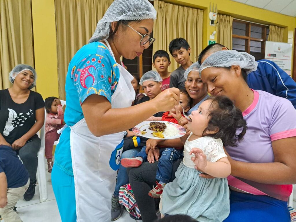 A nurse in Peru feeds a small child while others look on. MSH-Peru