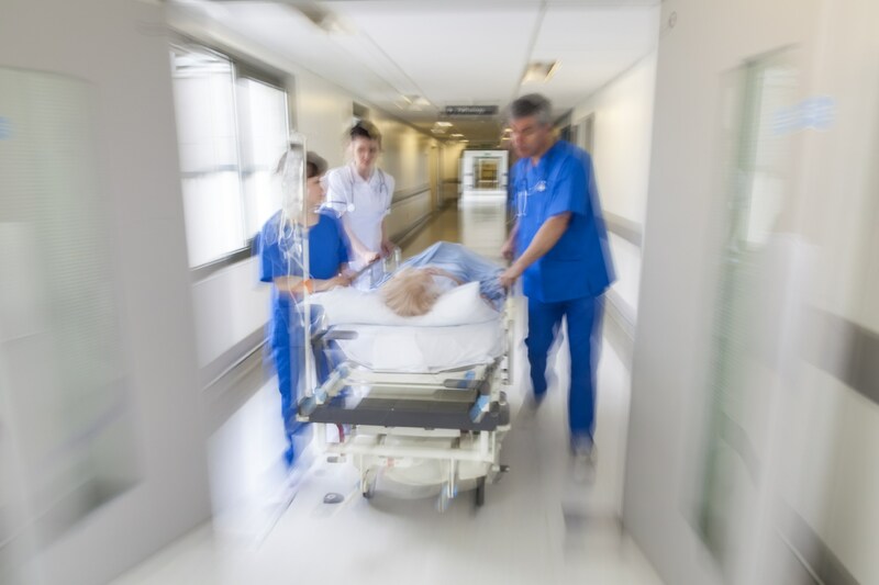 Blurred image of emergency room doctors and nurses in blue scrubs rushing a patient on a gurney down a corridor.