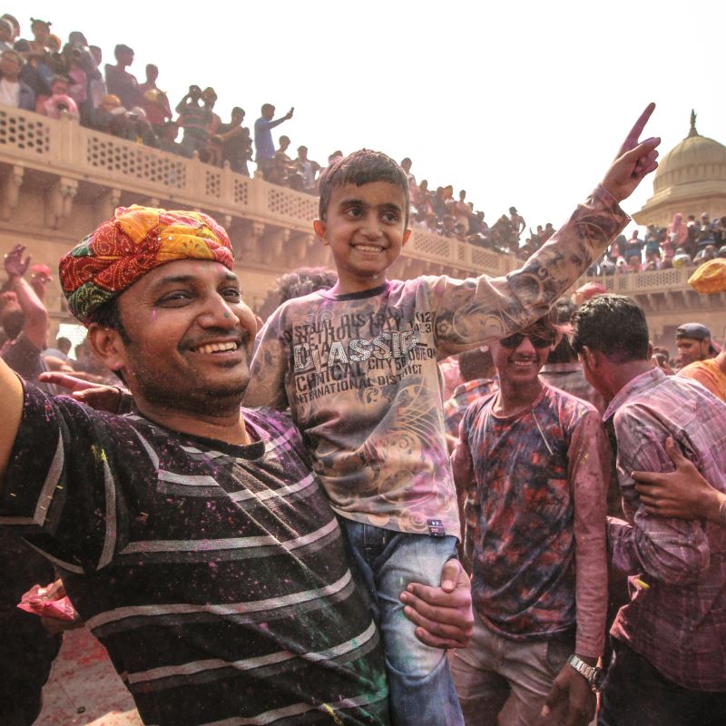 Un hombre sostiene a un niño en sus brazos. Ambos sonríen y levantan los brazos durante un festival.