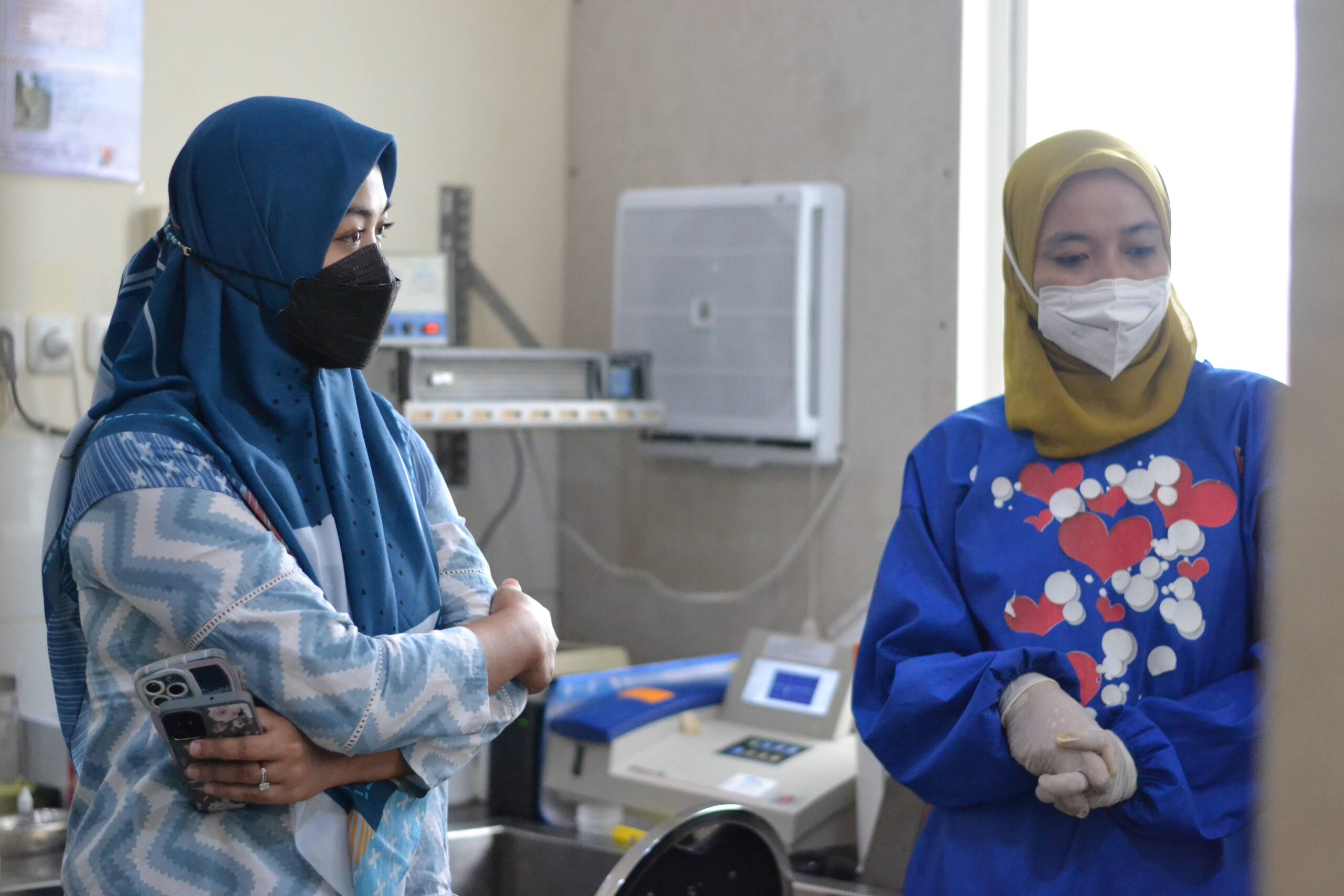 Duas mulheres com máscaras faciais e hijabs analisam dados sobre TB num centro médico na Indonésia.