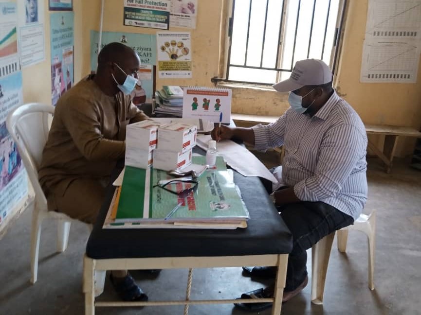 Dois homens discutem a logística de transporte de um carregamento de produtos contra a malária.