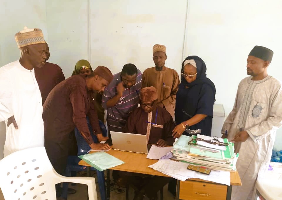 A group of people gather around a desk looking at a man working on a computer