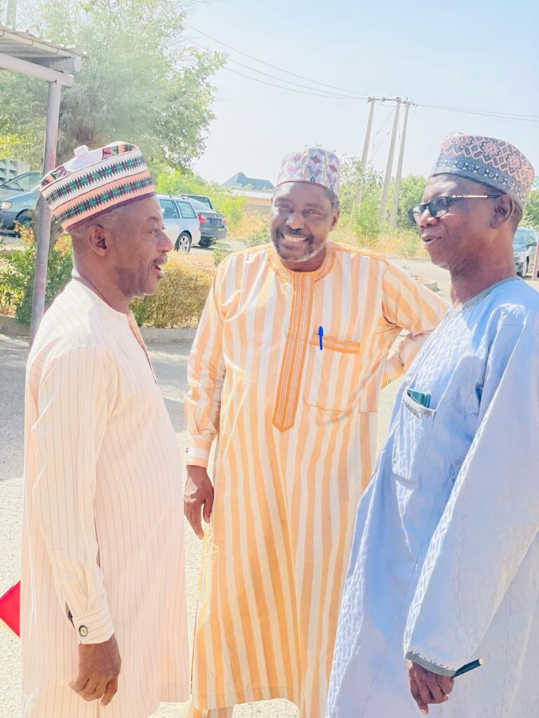 A group of three Nigerian men stand outdoors talking