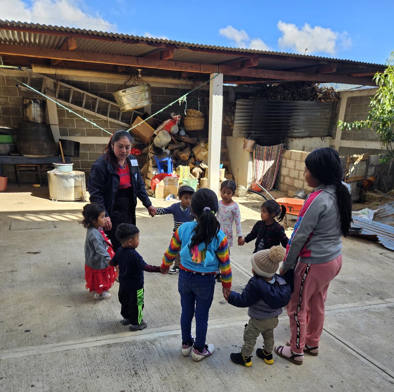 Two women lead a group of children playing a game outdoors.