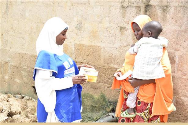 A community health worker distributes malaria medicines to a mother carrying her baby.